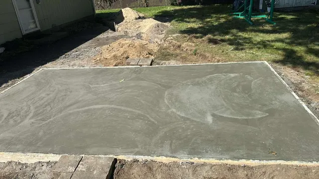 Newly poured concrete slab with forms in place and the excavated base visible along the edge