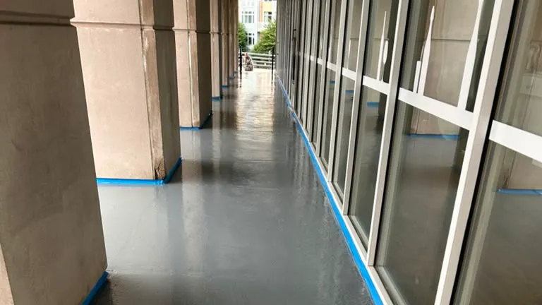 Freshly applied gray floor coating on a covered commercial walkway, with edges taped along the columns and storefront glass